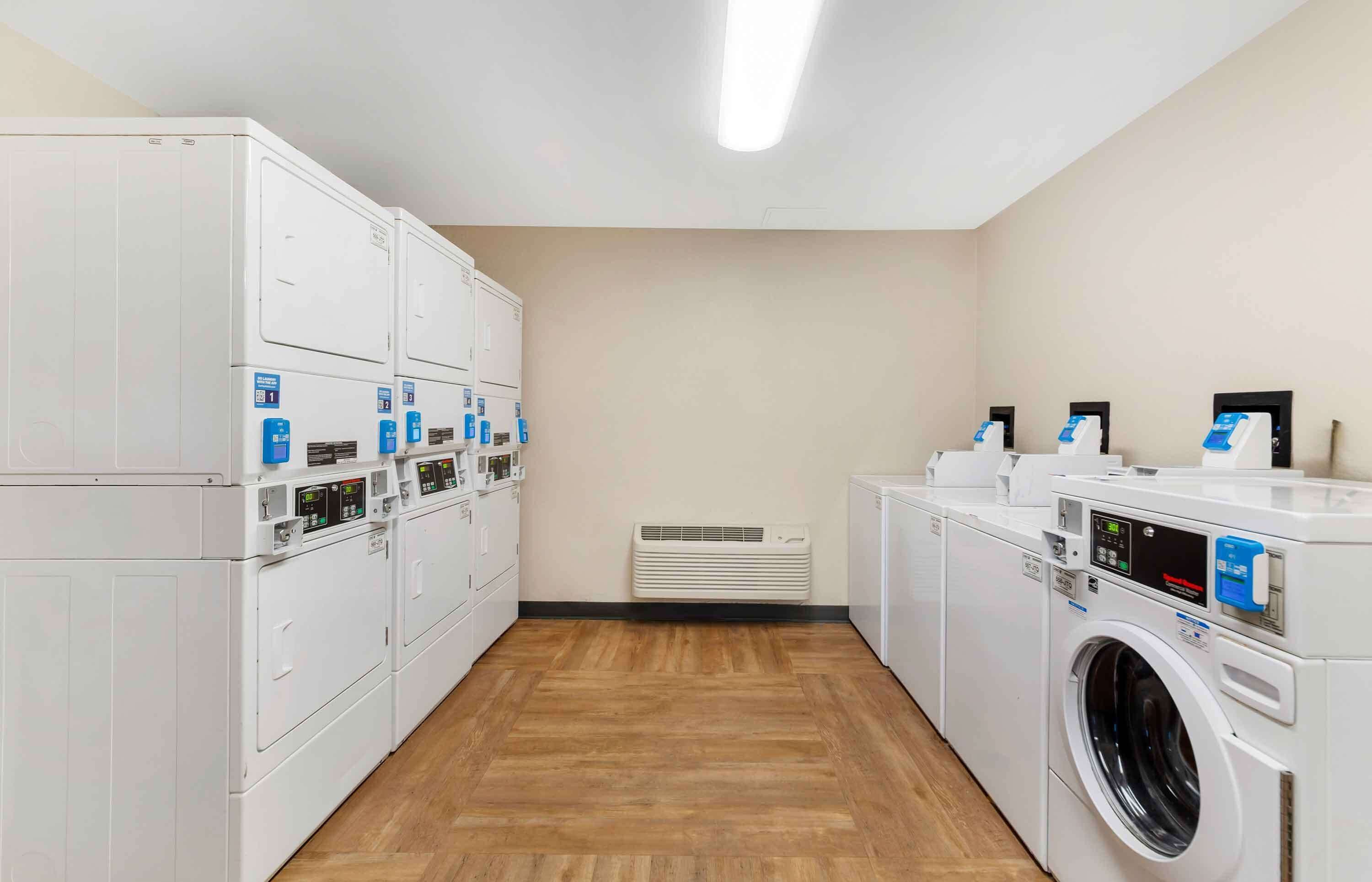 A laundry facility with multiple washing machines and dryers, a ventilation system, and a wooden floor.