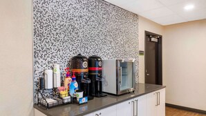 Un espace d’accueil d’hôtel doté d’un coin café comprenant deux machines à café, un réfrigérateur et divers produits à base de café et de thé.