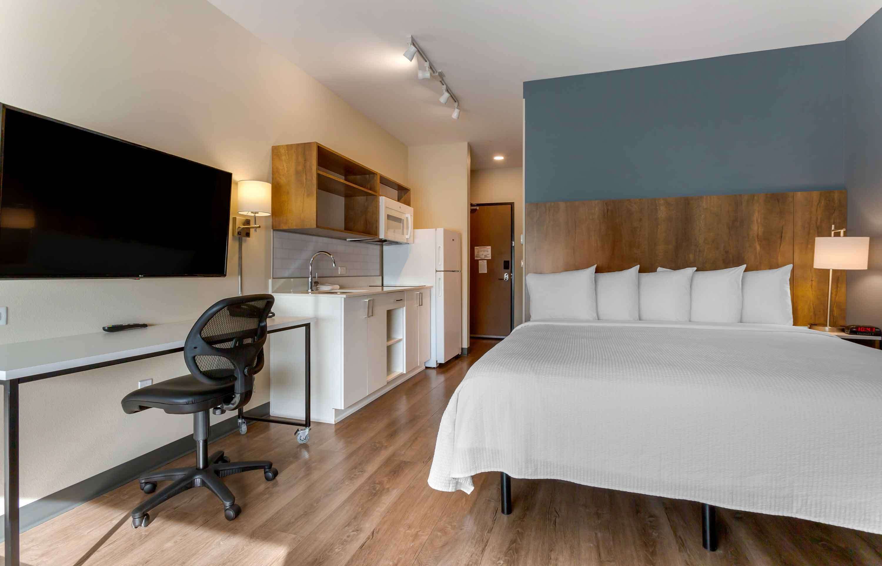 Een moderne hotelkamer met een groot bed, een bureau met stoel, een flatscreen televisie, een magnetron en een houten hoofdbord.