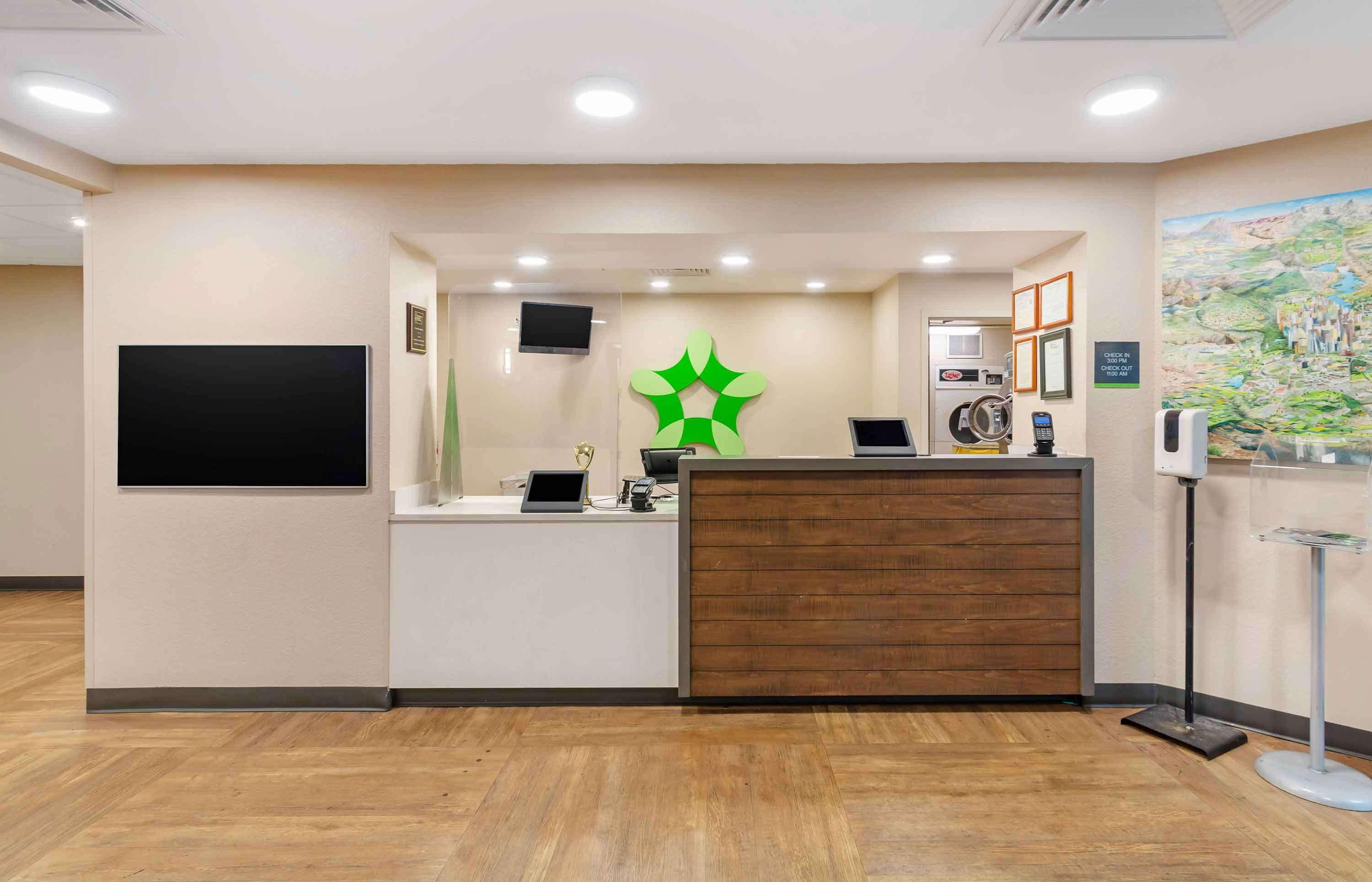 A reception area with a wooden reception desk, a green decorative wall piece, a mounted television, and a framed picture on the wall.
