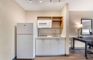 Una cocina pequeña con refrigerador, microondas, lavamanos y estantes de madera.