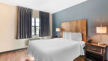 A hotel room with a large bed, a wooden headboard, two bedside tables with lamps, a large mirror, and a window with curtains.