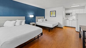 A hotel room with two beds, a kitchenette, and a blue accent wall. - Birch Hill Suites Kansas City – Independence (Independence)