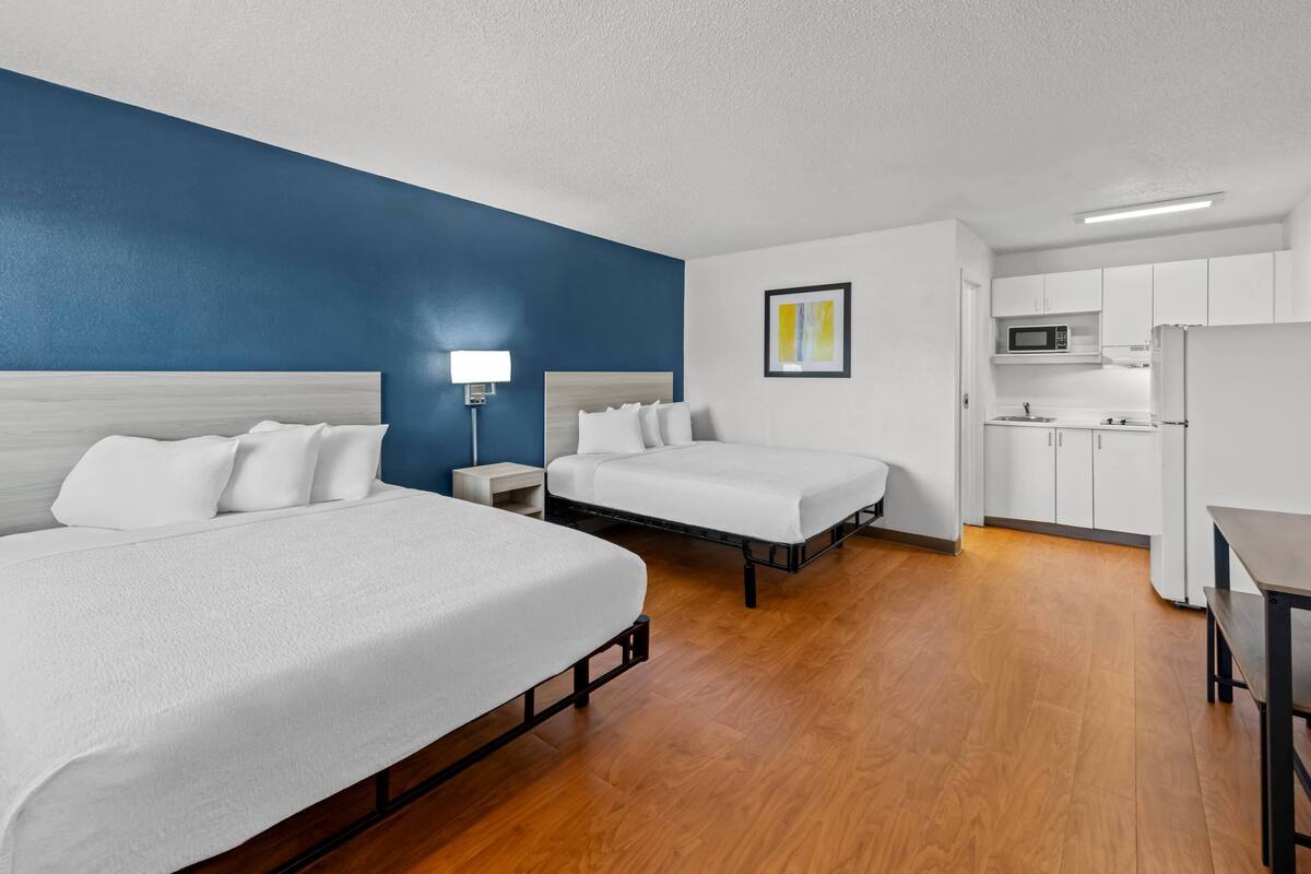 Ein Hotelzimmer mit zwei Betten, einer Küchenzeile und einer blauen Akzentwand.
