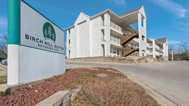 A multi-story hotel with a sign for Birch Hill Suites. - Birch Hill Suites Kansas City – Independence (Independence)