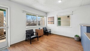 A spacious room with wooden flooring, two black leather chairs, a small wooden table, and a wicker basket with plants. - Birch Hill Suites Kansas City – Independence (Independence)