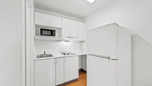 A compact kitchen with white cabinets, a microwave, a sink, and a refrigerator. - Birch Hill Suites Kansas City – Independence (Independence)