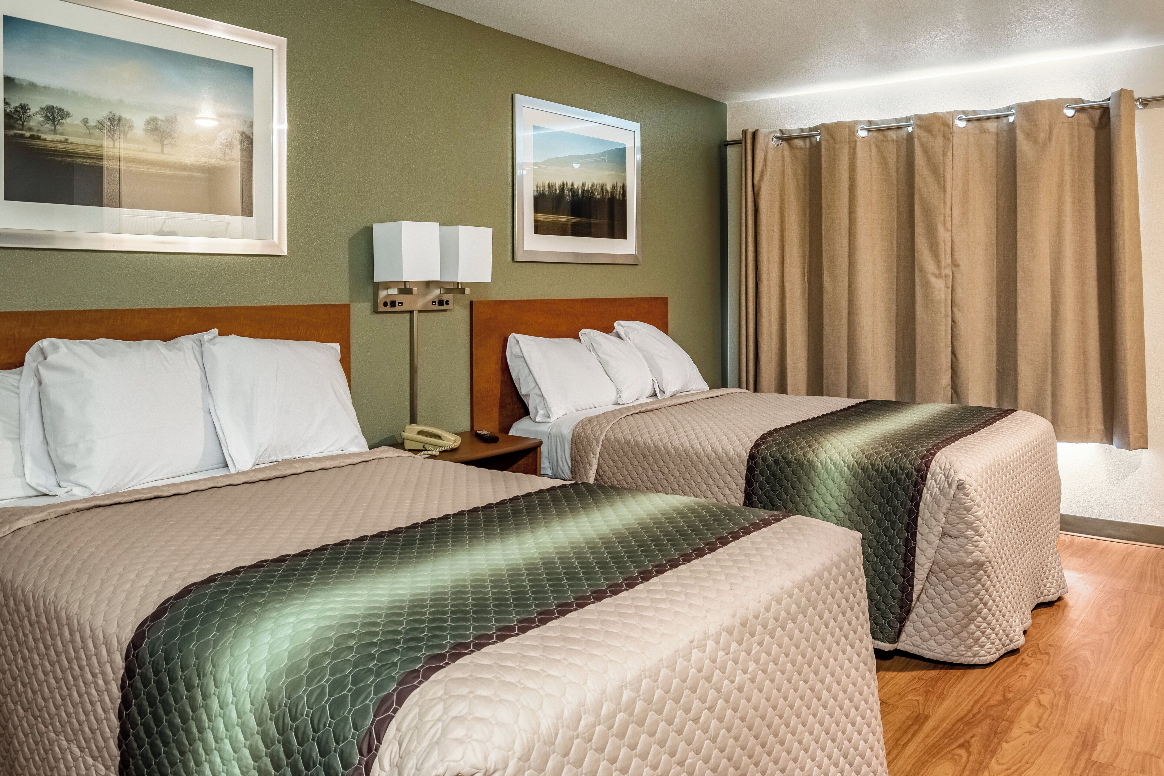 Quarto de hotel com duas camas, uma mesinha de cabeceira, uma luminária e duas fotos emolduradas na parede.