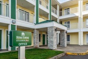 Un edificio de varios pisos con una combinación de colores verde y blanco, que presenta un letrero que dice “HomeTownne Studios by RealRoof Office” en la entrada.
