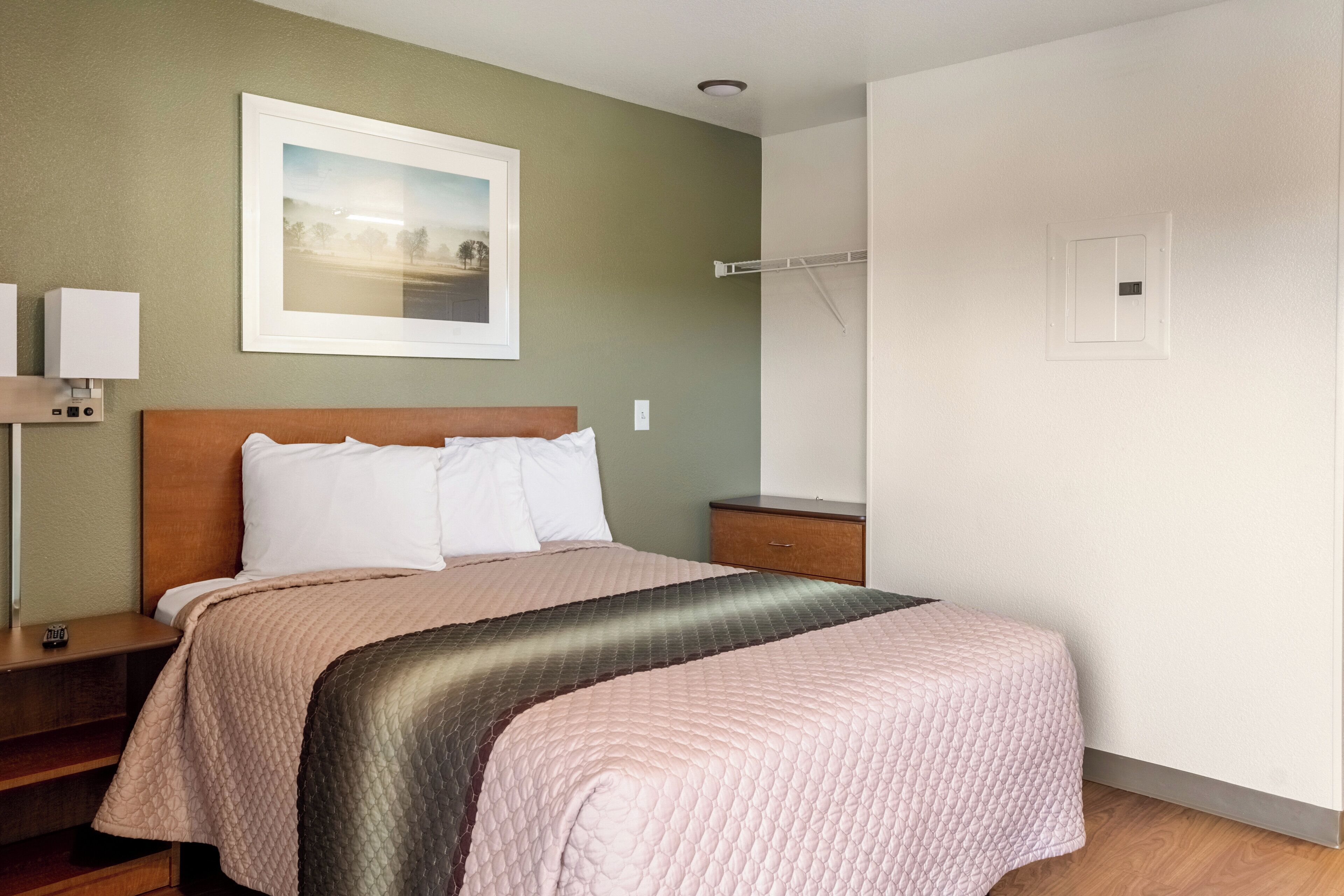 Una habitación de hotel con cama, mesitas de noche, una lámpara de pared y un cuadro enmarcado.