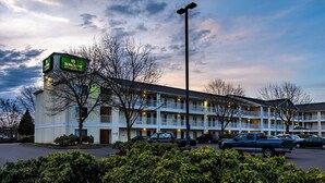 A motel with a green sign, multiple balconies, and a parking lot. - HomeTowne Studios By Red Roof Eugene - Springfield (Springfield)