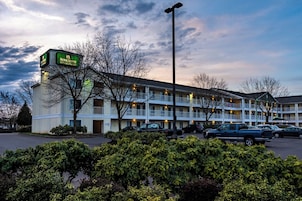 A motel with a green sign, multiple balconies, and a parking lot.