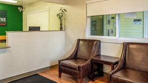 A reception area with a green wall, a reception desk, a potted plant, and two leather chairs. - HomeTowne Studios By Red Roof Eugene - Springfield (Springfield)