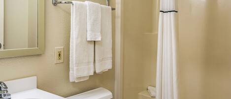 A bathroom with a white sink, a mirror, a towel rack with two towels, a shower curtain, and a toilet.