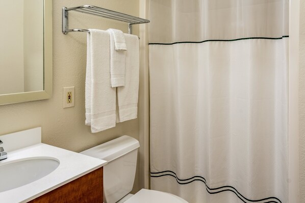 A bathroom with a white sink, a mirror, a toilet, and a shower curtain. - HomeTowne Studios By Red Roof Eugene - Springfield (Springfield)