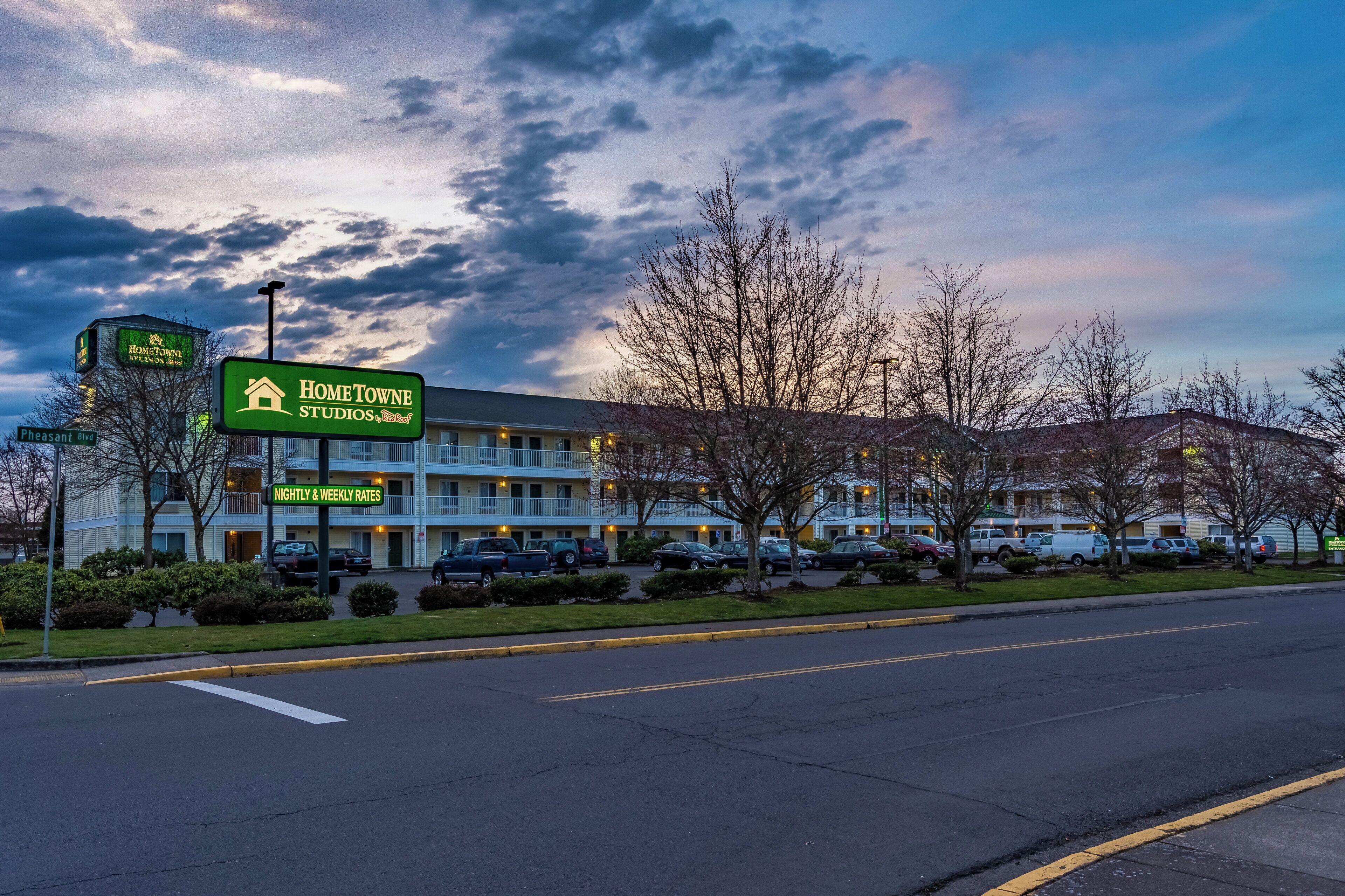 A motel with a sign indicating nightly and weekly rates, a parking lot, and a building with a flat roof.