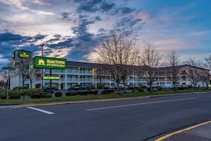 A motel with a sign indicating nightly and weekly rates, a parking lot, and a building with a flat roof. - HomeTowne Studios By Red Roof Eugene - Springfield (Springfield)