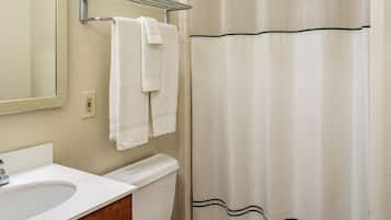 A bathroom with a white sink, a mirror, a towel rack with two towels, a toilet, and a shower curtain with a wavy pattern.