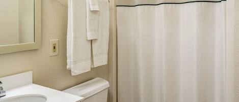 Une salle de bain avec un lavabo blanc, un miroir, un porte-serviettes avec deux serviettes, des toilettes et un rideau de douche à motifs ondulés.