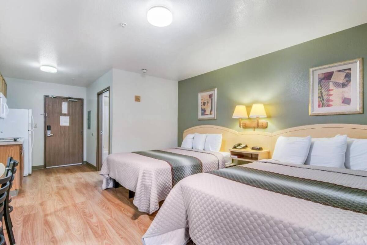 A hotel room with two beds, a desk, and a chair. There are two bedside tables with lamps.