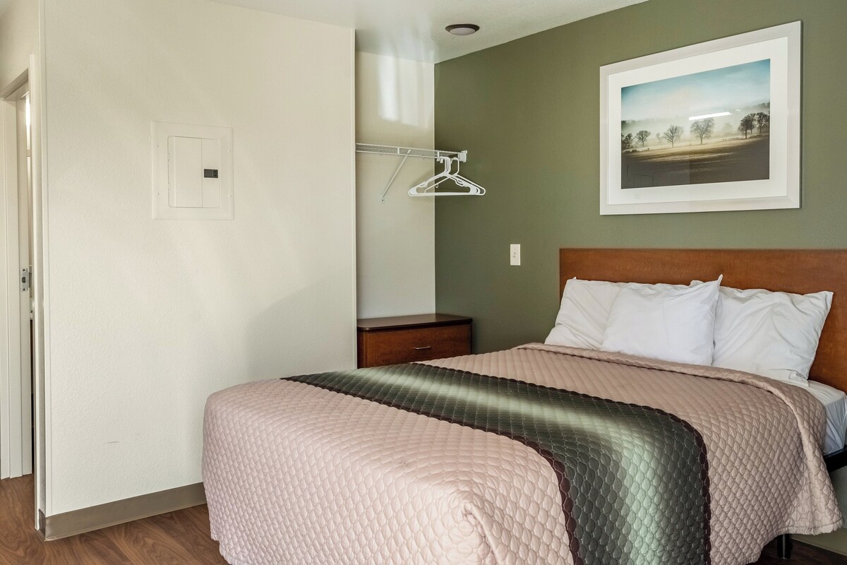 A bedroom with a bed, a nightstand, a wall-mounted coat rack, and a framed picture on the wall.
