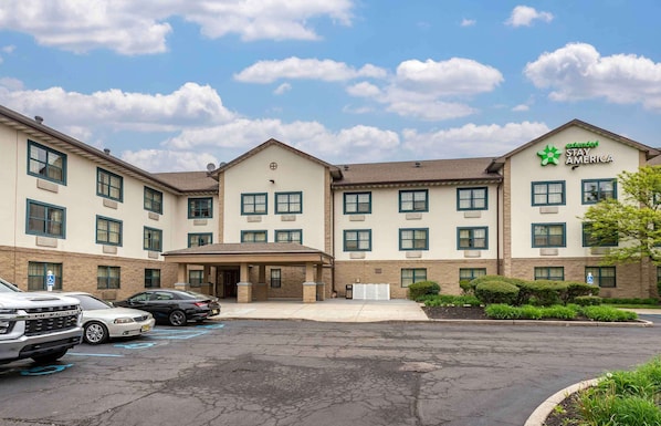 A Stay America hotel with a parking lot, multiple buildings, and a clear sky.