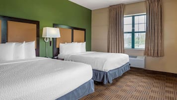 Une chambre d’hôtel avec deux lits, une grande fenêtre avec des rideaux, une lampe fixée au mur et un appareil de climatisation.