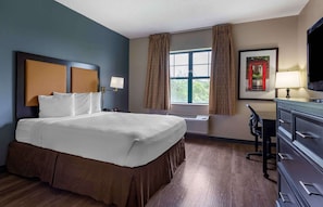 A hotel room with a large bed, a desk with a chair, a flat-screen TV, and a window with curtains.