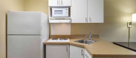 A compact kitchen with a refrigerator, microwave, stove, sink, and white cabinets.
