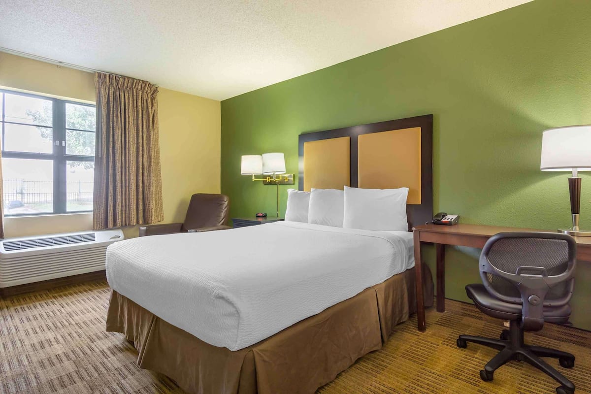 Een hotelkamer met een groot bed, een bureau met stoel, een lamp en een raam met gordijnen.