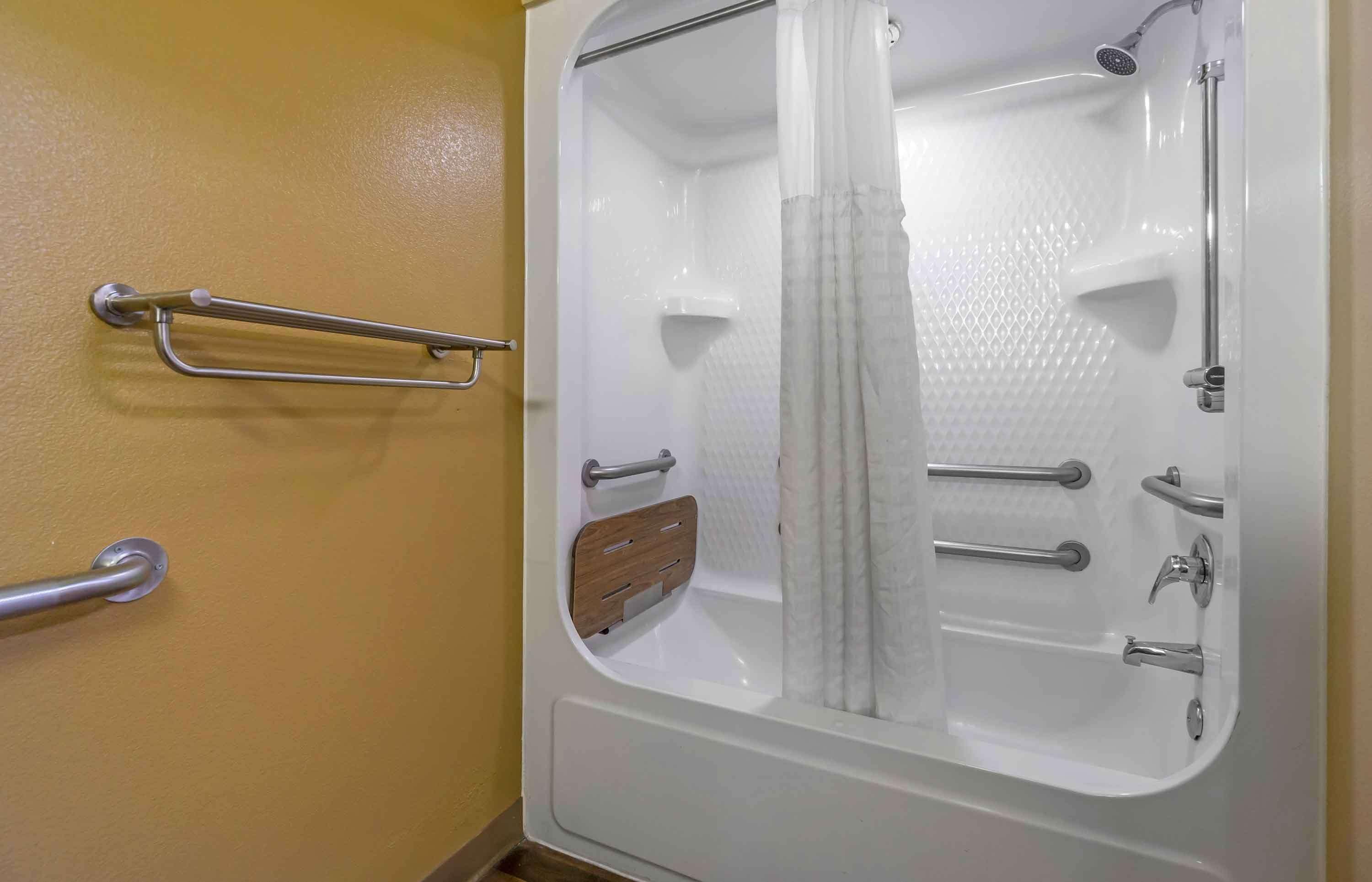 Un baño con bañera, ducha y retrete. Se han instalado barras de apoyo en las paredes.