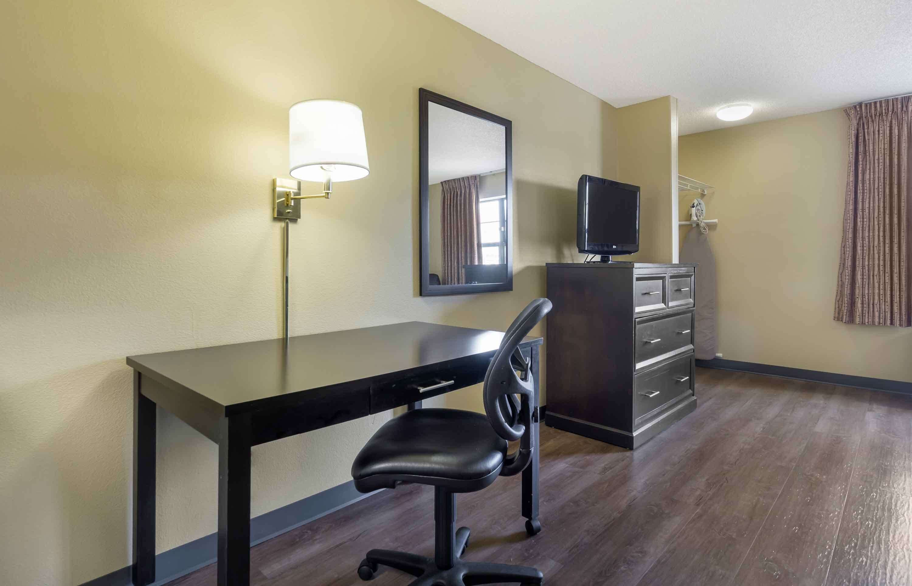 Una habitación de hotel con escritorio, silla, televisor, cómoda y lámpara.