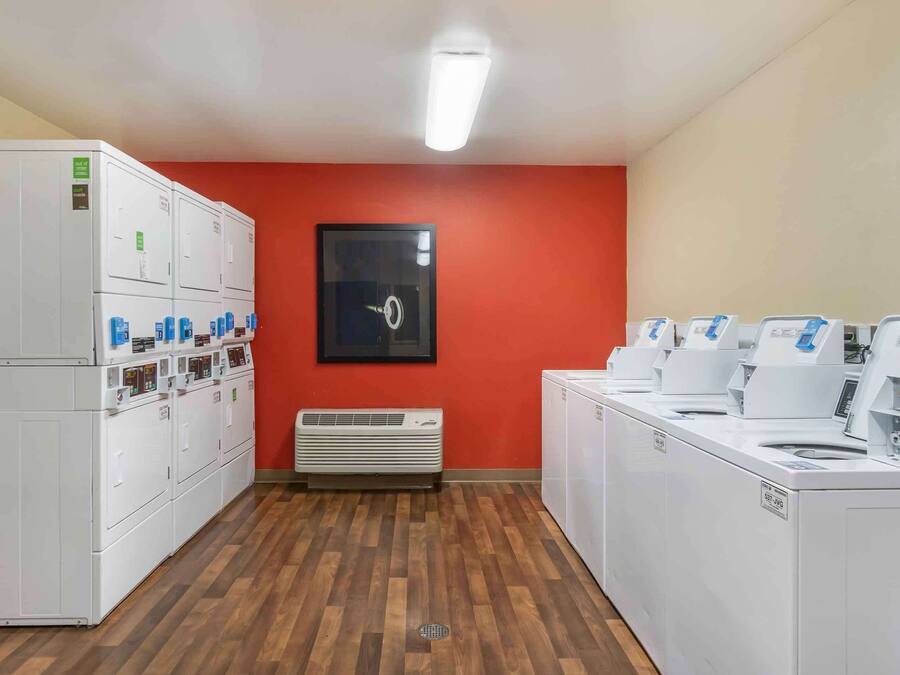 A laundry room with multiple washing machines and dryers, a vent, and a red wall.