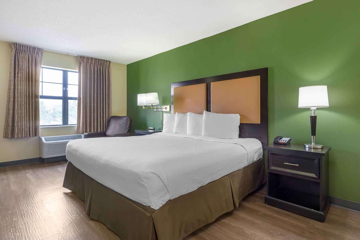 Hotelkamer met een groot bed, twee bedlampen, een stoel, een nachtkastje met telefoon en een raam met gordijnen.