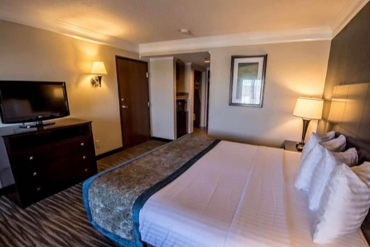 A hotel room with a bed, a TV, a desk, and a door leading to a hallway.