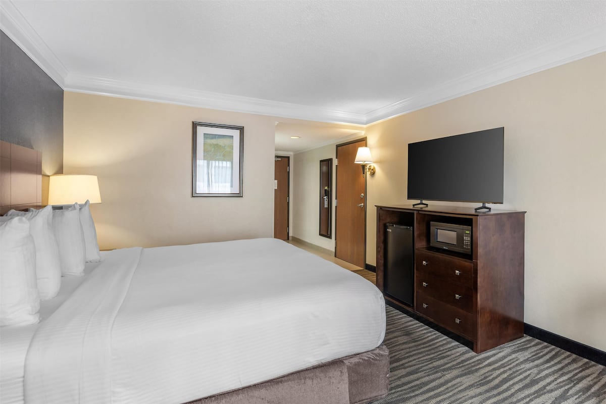 A hotel room with a large bed, a flat-screen TV, a desk with drawers, and a lamp.