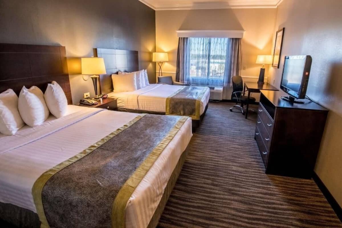 A hotel room with two beds, a desk, a television, and a window with curtains.