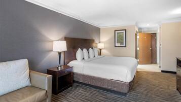 Une chambre d’hôtel avec un grand lit, deux tables de chevet avec des lampes, un canapé, un sol recouvert de moquette et une porte donnant sur une autre pièce.