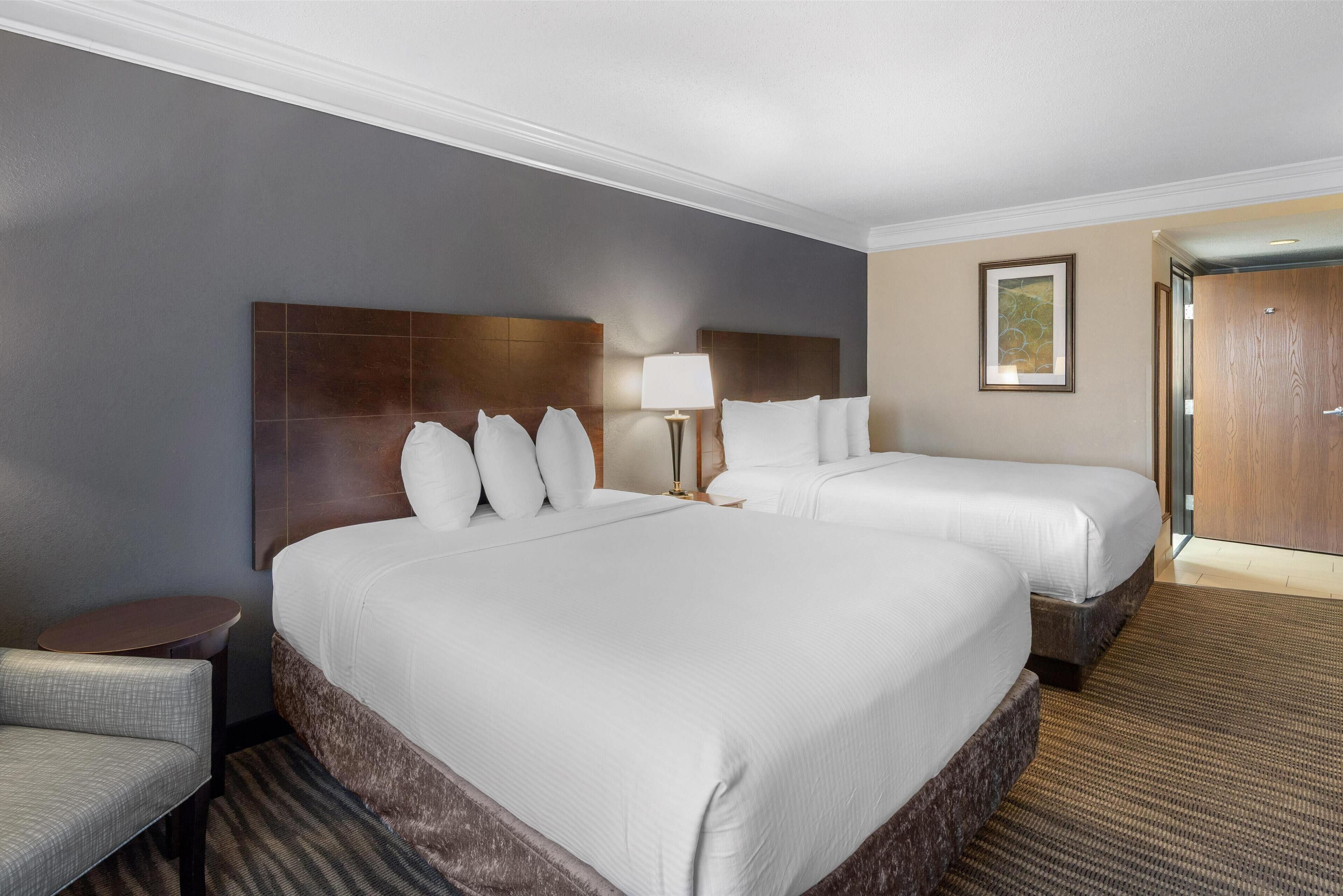 Una habitación de hotel con dos camas, una mesita redonda pequeña, una silla y una lámpara.
