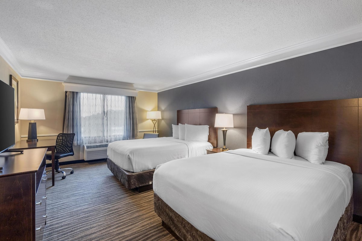 A hotel room with two beds, a desk, a chair, and a TV.