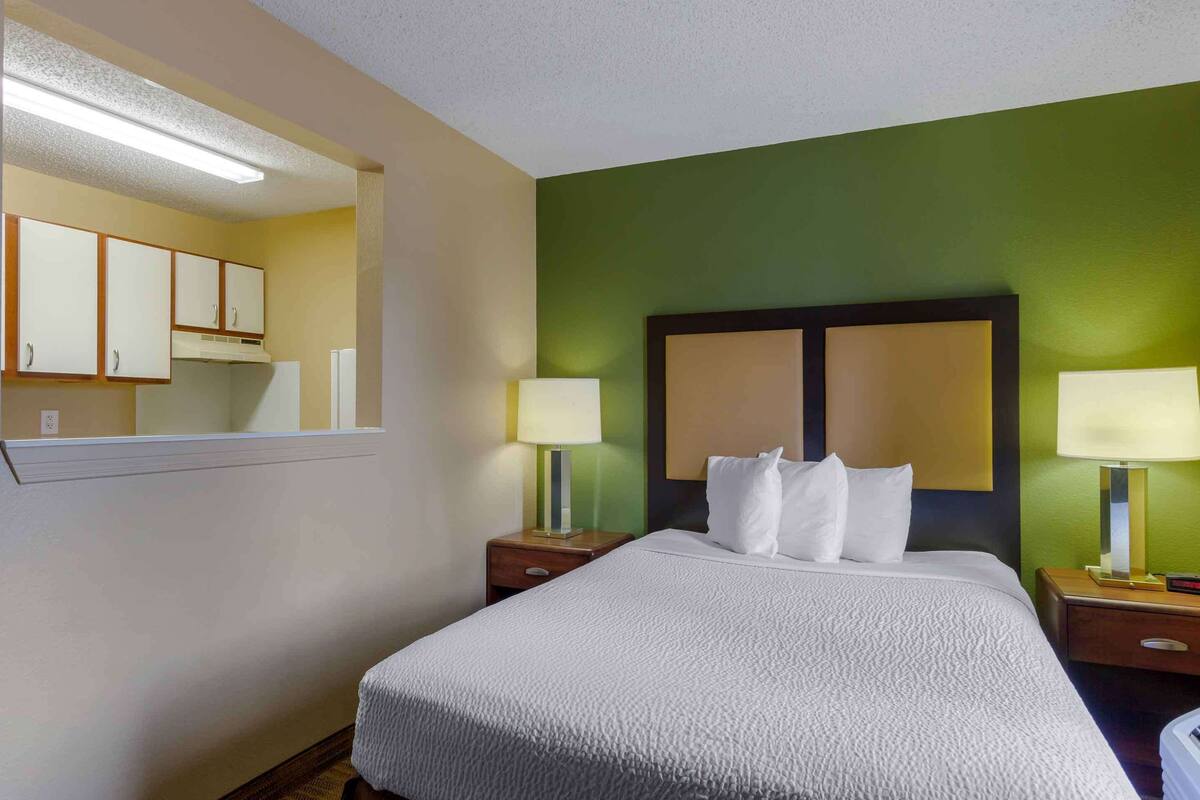 A hotel room with a bed, two bedside tables, a nightstand, a mirror, and a wall-mounted headboard.