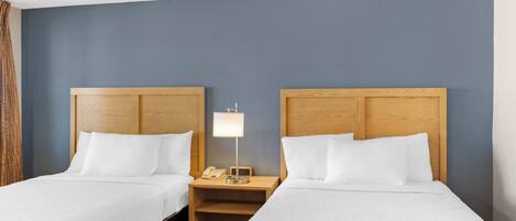 Een hotelkamer met twee bedden, houten hoofdborden, witte beddengoed, een nachtkastje met een lamp en een telefoon.
