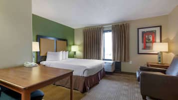 Una habitación de hotel con una cama, un escritorio, una silla, una lámpara y un cuadro en la pared.