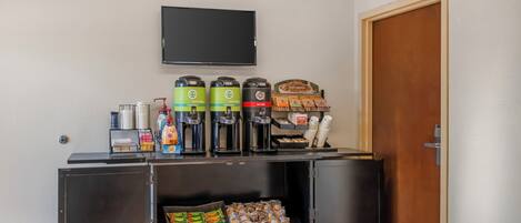 A kitchenette with a coffee station, snack bar, and a flat-screen TV mounted on the wall.