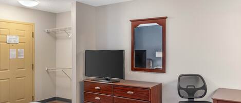 Een hotelkamer met een bed, een houten dressoir met een flatscreen televisie, een spiegel, een stoel en een bureau.