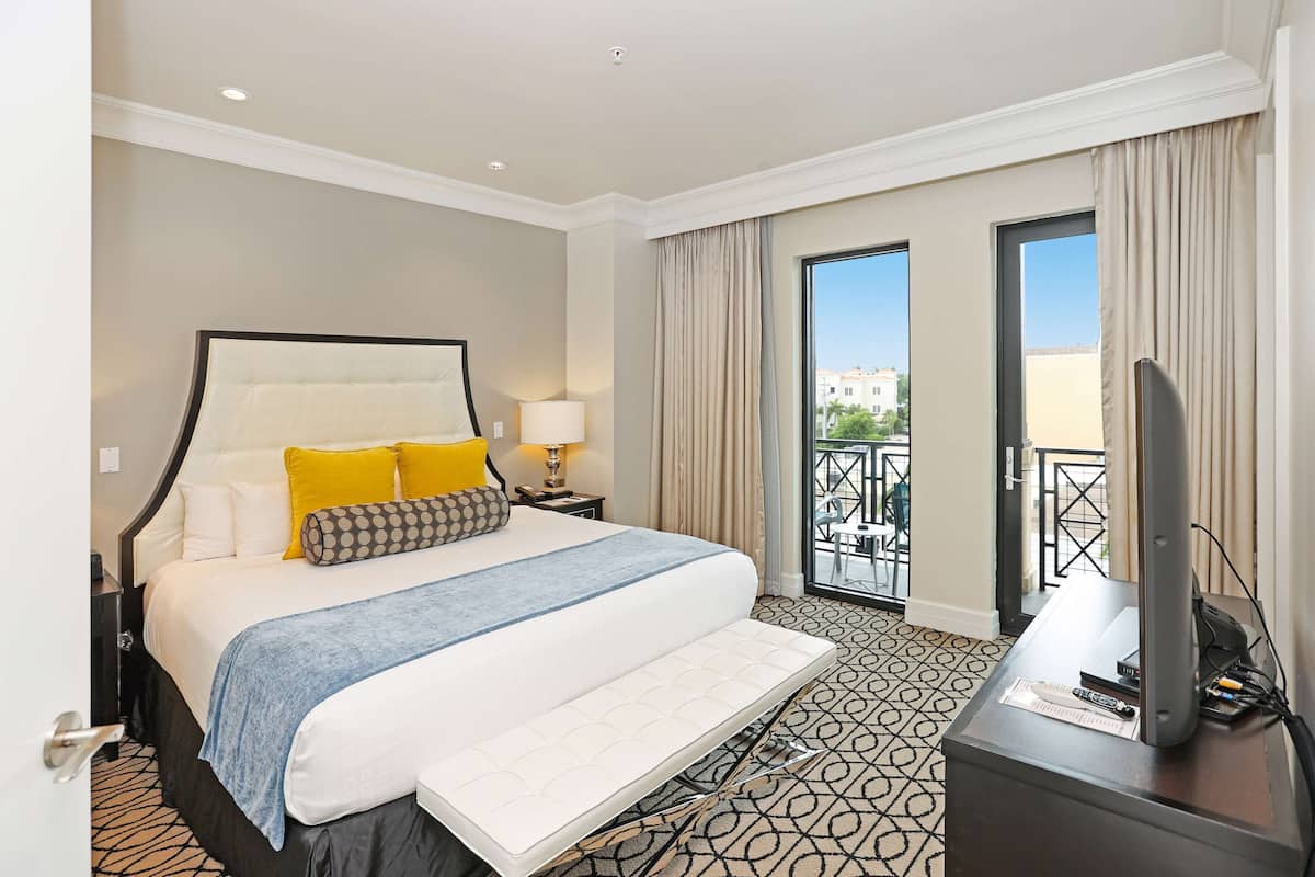 A hotel room with a large bed, a TV, and a balcony with a view.