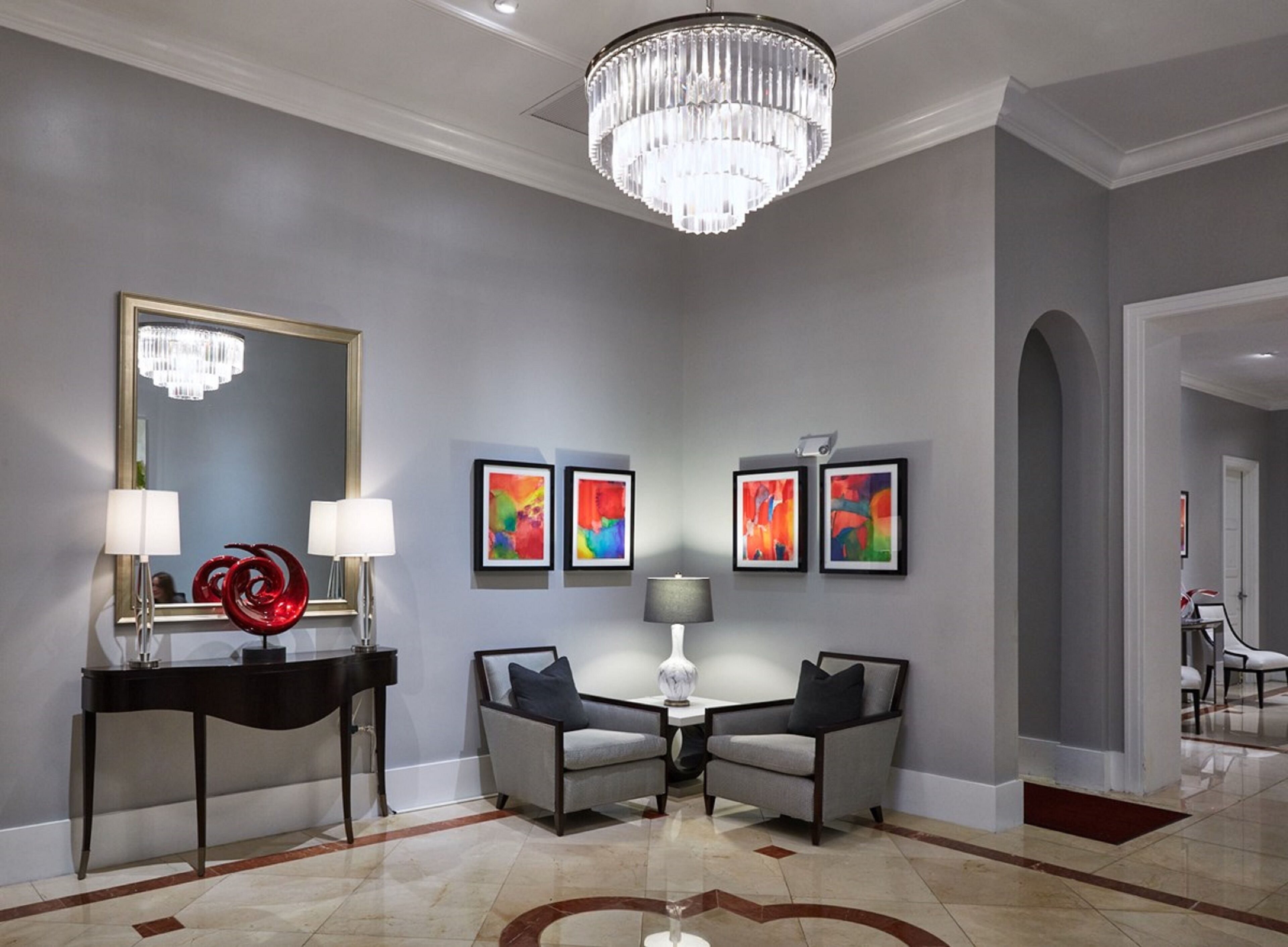 A modern lobby with a chandelier, two armchairs, a console table, a mirror, and abstract art on the wall.