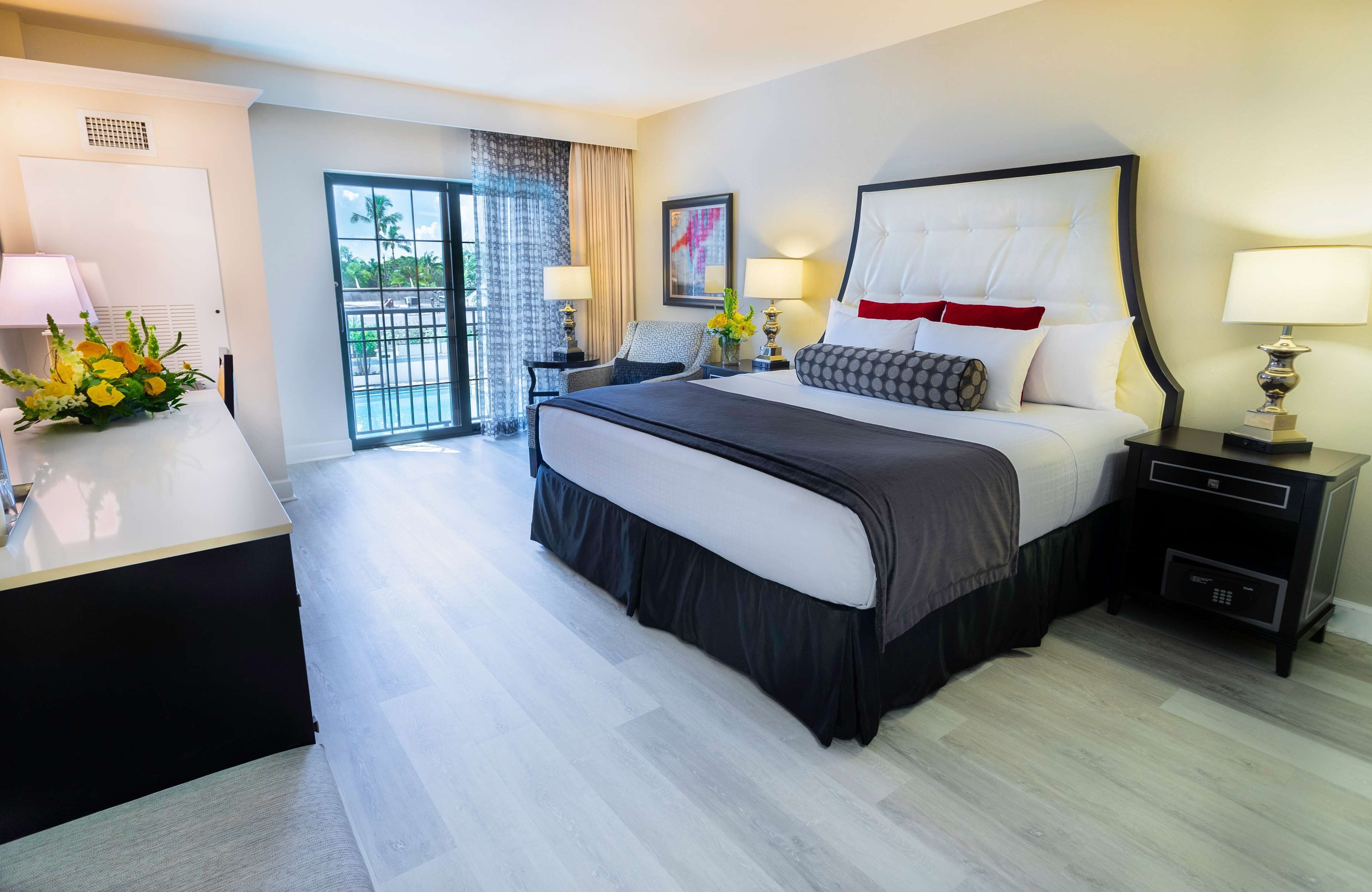 Une chambre d’hôtel avec un grand lit, deux tables de chevet avec des lampes, un bureau avec une lampe, une chaise et une vue sur l’extérieur grâce à une porte coulissante.