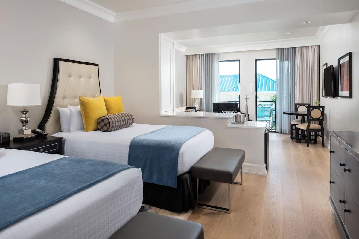 A hotel room with two beds, a desk, a TV, and a balcony with a view.