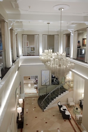 A spacious, multi-level hotel lobby with a grand chandelier, a staircase, and a seating area with modern furniture.